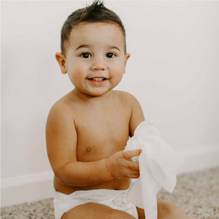 Baby wearing a diaper holding a single white wipe with a neutral colored background