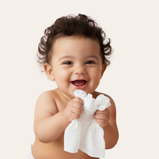 Baby holding a white wipe against a plain background
