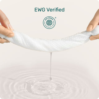 A pair of hands stretches a white, porous, gel-like fabric strip over a surface with water droplets dripping from it. The text 'EWG Verified' and a circular certification logo are displayed at the top against a clean, light beige background.
