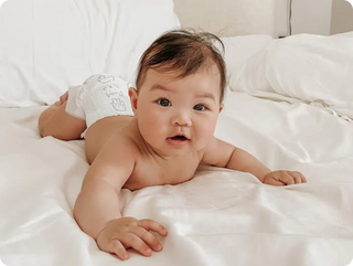 Baby lying on a white bed wearing a diaper
