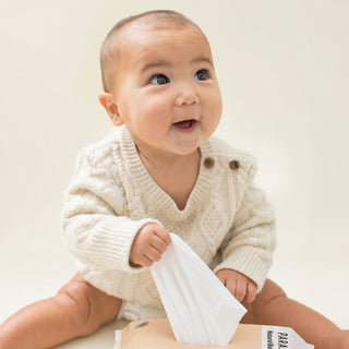 Baby wearing a cream knitted sweater holding a wipe
