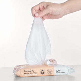 Hand pulling a baby wipe from a Parasol brand packaging on a light background

