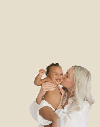 Woman holding a baby against a beige background
