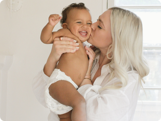 Woman kissing a baby on the cheek in a bright room
